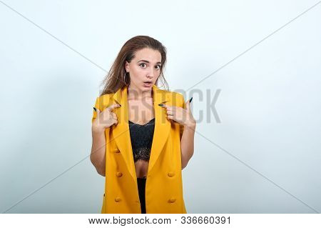 Attractive Young Woman In Yellow Jacket Pointing Finger On Herself, Loooking Confused Isolated On Gr