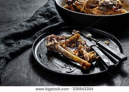 A Plate Of Chicken Bones And A Chicken Skeleton In A Baking Dish. Leftovers From Dinner. Black Backg