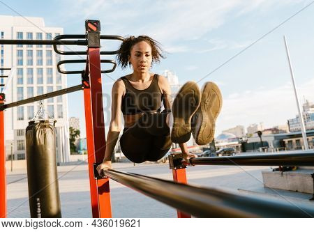 Concentarted young fit african fitness woman exercising on parallel bars at the sportsground