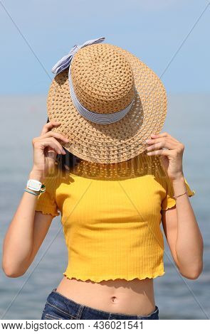 Young Girl Covers Her Face With Straw Hat At The Sea In Summer