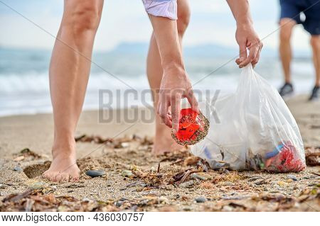 Close-up Of A Womans Hands Picking Up Plastic Trash Into A Bag On The Beach