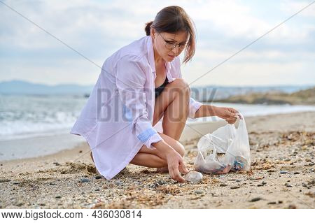 Mature Woman Tourist Relaxing On The Beach Collecting Plastic Trash In A Bag