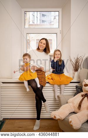Happy Portrait Of Aunt With Her Little Nieces Sitting On The Window At Home