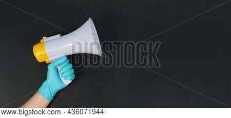 Megaphone In Hand And Wearing Blue Latex Glove On Black Background. Studio Shooting.