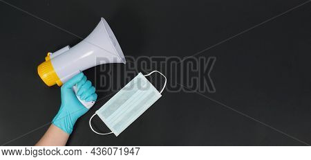 Megaphone In Hand And Wearing Blue Latex Glove And Face Mask On Black Background. Studio Shooting.
