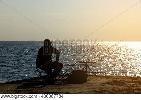 A Fisherman Is Fishing With Afishing Rod On The Seashore, Opposite The Sun. High Quality Photo