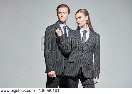 Fashion shoot. Stylish couple of young people man and woman in elegant striped pantsuits. Studio portrait on a gray background. Impeccable look. Men's clothing style.