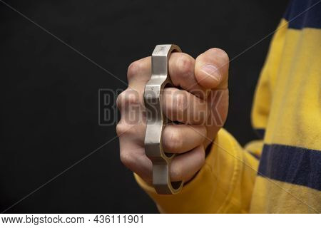 Male Hand Squeezes Metal Brass Knuckles On A Black Background.  Concept: Grievous Injuries And Injur