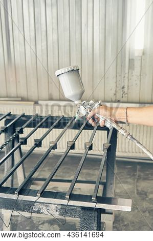 Woman Worker Paints Forged Balusters In Black Color With Spray Gun On Rack Support In Contemporary S