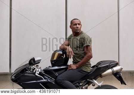 Young black man sitting on sports motorcycle on city street. Guy wearing casual clothes. Concept of trip and journey in personal transport. Vacation, leisure, hobby and enterteiment. Idea of freedom.