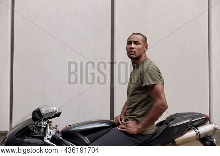 Young mixed race man sitting on sports motorcycle on street. Concept of trip and journey in personal transport. Guy wearing casual clothes. Vacation, leisure, hobby and enterteiment. Idea of freedom.