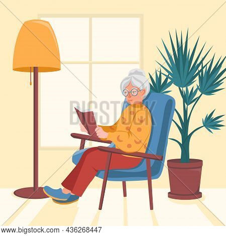 Granny Sits In A Chair Near The Window And Reads A Book. An Old Woman Is Resting. A Floor Lamp And A