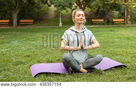 Young Fitness Woman Meditates While Sitting Tna Mat In The Park. Slim Woman Practicing Yoga Pose. He