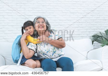 An Elderly Asian Grandmother And Her Granddaughter Is 6-year-old Sitting On White Sofa, Are Hugging,