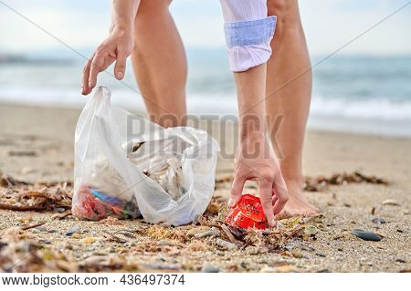 Close-up Of A Womans Hands Picking Up Plastic Trash Into A Bag On The Beach