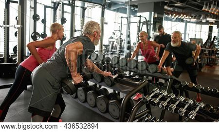 Back View Fit Senior Couple Working Out In Gym, Lifting Weights, Leaning On Rack With Dumbbells. Str