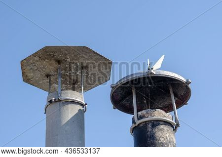 Smoke Pipes With Canopies Against The Blue Sky. Two Asbestos-cement Pipes. Chimney Canopies In Black