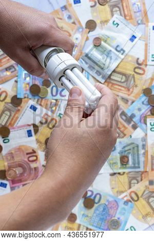 Electricity Costs: Person Changing Light Bulb Saving More Electricity With Background Of Euro Bankno