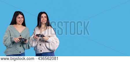 Banner, Long Format. Twin Sisters Play Online Games. The Girls Are Holding Joysticks In Their Hands 