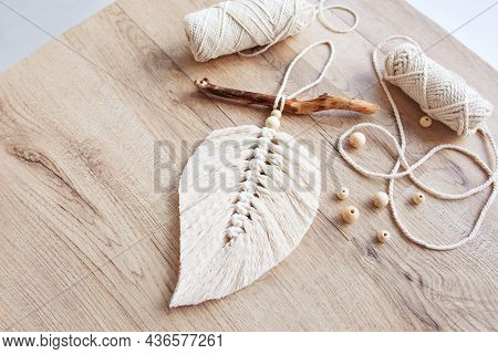 Macrame Leaf  In Natural Color And Thread Windings Lying On A Wooden Table. Cotton Rope Decor Macram