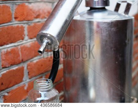 A Drop Of Alcohol Distillation Dripping Into A Bottle From A Tube Of A Moonshine Still Against A Bri