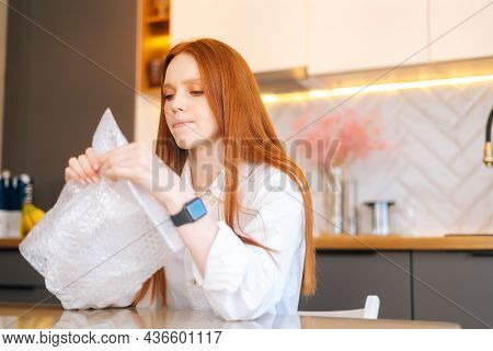 Close-up Face Of Stressed Young Woman Playing Pops Bubble Wrap To Calm Herself Sitting At Table In K