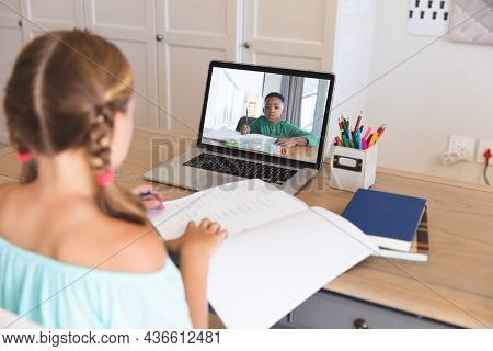 Caucasian girl using laptop for video call, with elementary school pupil on screen. communication technology and online education, digital composite image.