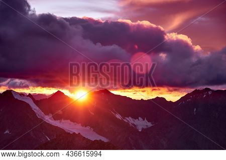 Sunset In Mountains. Reflection Of Red Sun On Mountain Snow Peaks And Clouds. Altai, Belukha Area