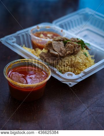 Roasted Meat Served With Rice And Chillies Tamarind Sauce And Curry Gravy In A Take Out Container. M