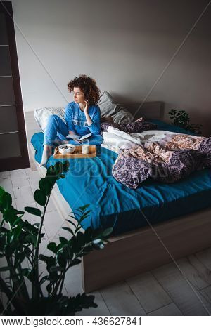 Caucasian Woman Sitting In Blue Pajamas In Bed Looking Back And Falling To Thoughts While A Healthy 