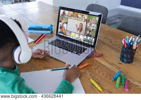 African american boy using laptop for video call, with diverse elementary school pupils on screen. communication technology and online education, digital composite image.