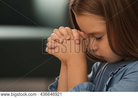 Cute Little Girl With Hands Clasped Together Praying On Blurred Background, Closeup