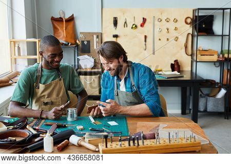 Portrait Of Smiling Male Artisan Teaching Young Apprentice In Leatherworkers Workshop, Copy Space
