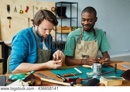 Portrait Of Modern Male Artisan Teaching Young Apprentice In Leatherworkers Workshop, Copy Space