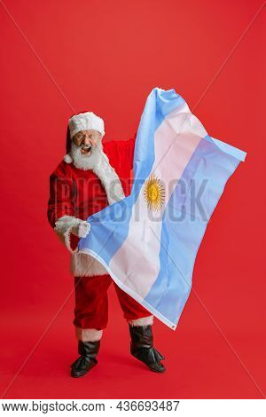 Full-length Portrait Of Senior Man Wearing Santa Claus Costume, Holding Flag Of Uruguay Isolated Ove