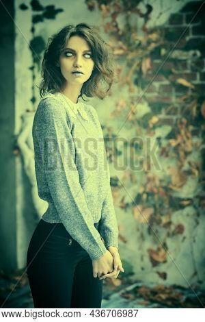 A sad lonely ghost girl with faded eyes and matted black hair stands among withered foliage looking at the camera. Horror film, thriller. Halloween.