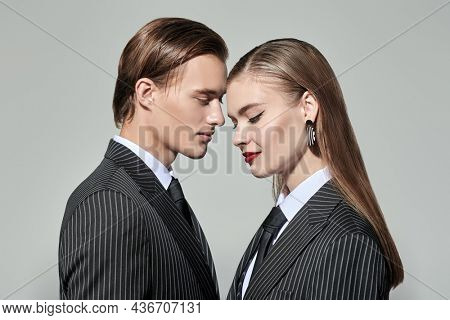 Stylish young couple in smart striped pantsuits poses on a gray studio background. Impeccable look. Business style. Fashion shot. 