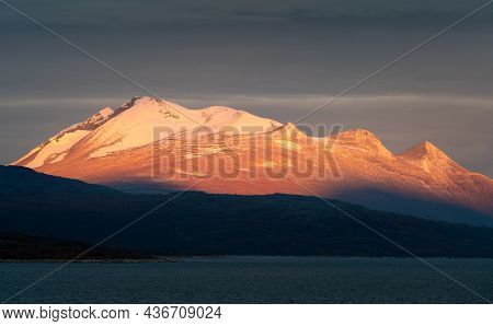 Epic Sunrise Light Illuminating Rocky, Glacier Covered Peak With Dark Cloudy Sky In The Background. 