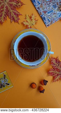 A Cup Of Tea, Maple Leaves, Acorns, A Notebook On An Orange Background. View From Above