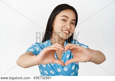 Portrait Of Brunette Asian Girl Smiling, Showing Heart Love Gesture And Looking Romantic At Camera, 
