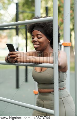 Young smiling female in sportswear scrolling in smartphone at break after hard training
