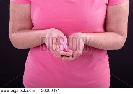 Midsection of caucasian woman in pink tshirt holding pink ribbon. breast cancer positive awareness campaign concept digitally generated video.