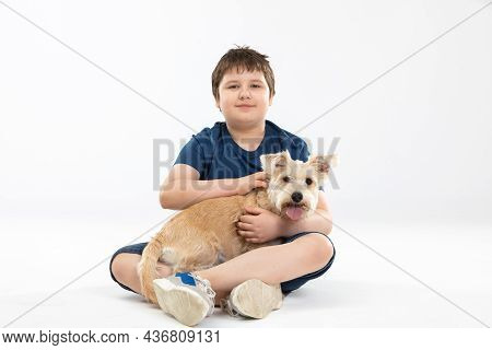 A Young Boy Sits On A White Background And In His Hands He Holds His Beloved Dog.