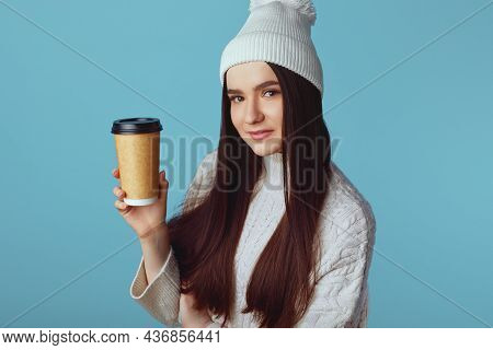 Cheerful Pretty Girl Wearing White Oversize Sweater And Hat Isolated Over Blue Backdrop, Holding Tak