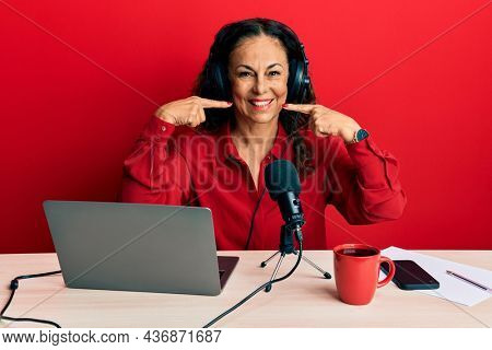 Beautiful middle age woman working at radio studio smiling cheerful showing and pointing with fingers teeth and mouth. dental health concept. 