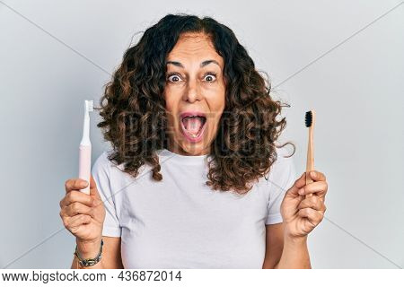 Middle age hispanic woman holding electric toothbrush and teethbrush celebrating crazy and amazed for success with open eyes screaming excited. 