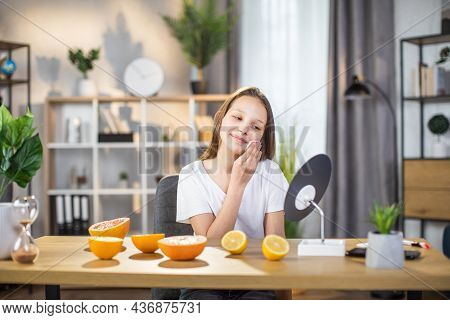 Pretty Female Teenger Sitting At Table While Cleaning Face With Cotton Pad And Looking At Mirror. Ha