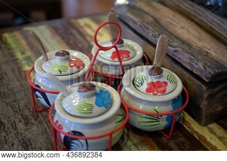 A Set Of Glazed Ceramic Condiments On An Old Patterned Wooden Table In A Noodle Shop.