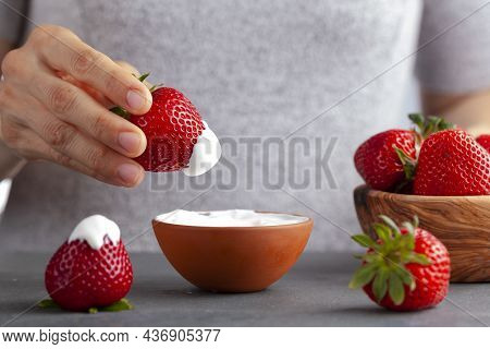 A Caucasian Woman Is Dipping A Fresh Ripe Strawberry Into Cream Or Yoghurt. Concept Image For Health