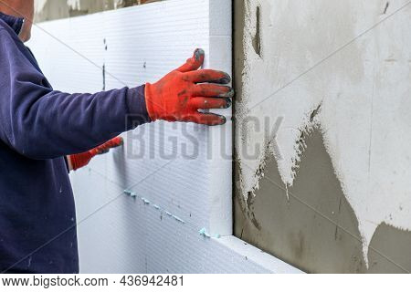 Construction Worker Installing Styrofoam Insulation Sheets On House Facade Wall For Thermal Protecti
